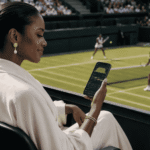 Woman at a tennis match checking a betting app on her phone while players compete on the court.